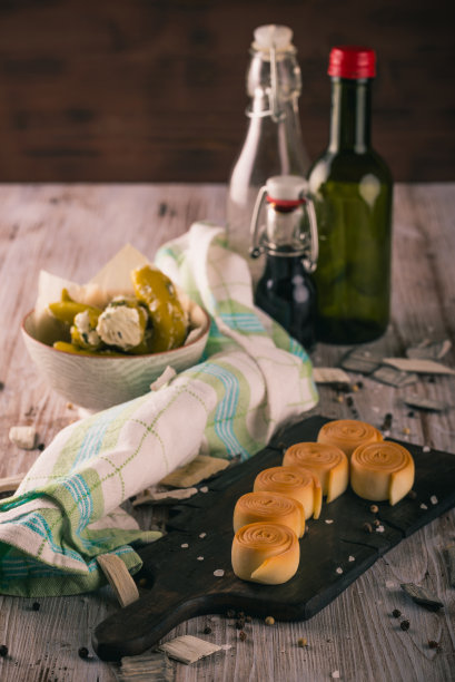 垂直的照片，几卷烟熏奶酪parenica放在黑色的乡村木板上，绿色的辣椒塞满奶酪和香草和少数瓶子在背景。图片下载