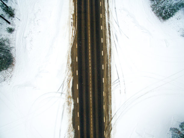 冬季森林和柏油路。从以上观点。这张照片是用无人机拍摄的。松树和云杉的森林里有一条黑色的路在雪地里图片下载