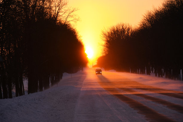 在暴风雪中，汽车在夕阳下行驶在冬日的雪道上图片下载