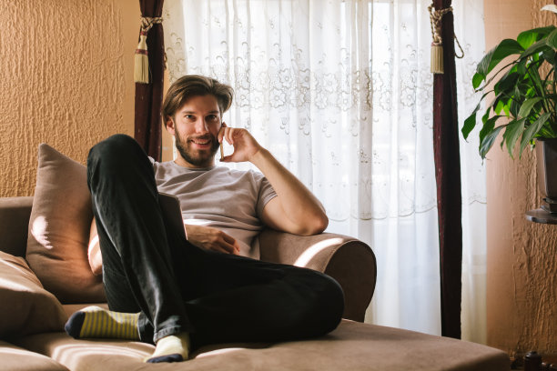 年轻人坐在客厅的沙发上打电话图片下载