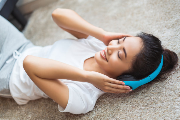 亚洲妇女正在听音乐，她在房间里愉快地睡在地毯上唱歌图片下载