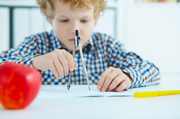 小男孩在纸上用分度器测量距离。素材图片
