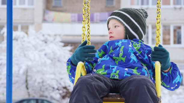 一个白人小男孩在冬天的操场上荡秋千。图片下载