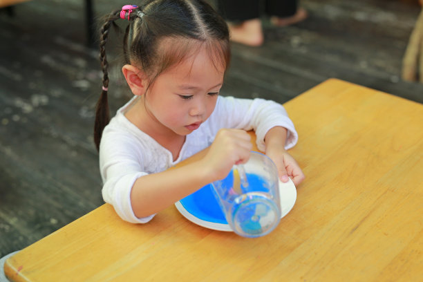 亚洲小女孩把溶液倒进盘子里。年轻科学家学习的科学实验。图片下载