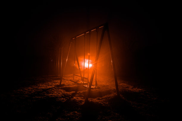夜间照片的金属秋千站在室外的时间与雾和超现实色调的灯光背景。没有人在那里。图片下载