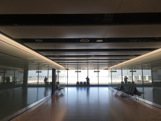 从机场走廊往下看，一名男子在机场的窗户背光下讲手机的剪影。商务旅行，机场内部的照片。图片下载