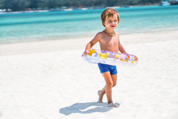 微笑的小男孩走在海滩上充气的戒指。素材图片