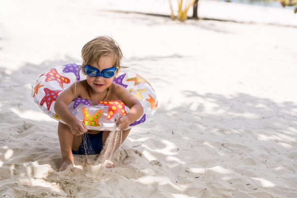 可爱男孩带着游泳圈和护目镜在沙滩上玩耍素材图片