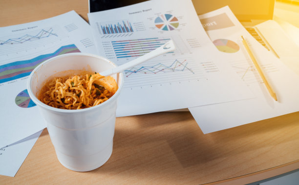 办公室工作桌上的杯面，白纸是文件计划总结报告，电脑笔记本上的纸。素材图片