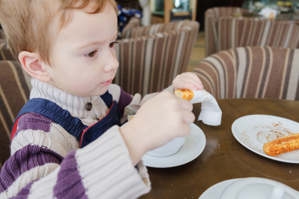小男孩在咖啡馆里用杯子里的饼干和蛋糕喝茶。素材图片