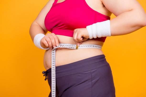 不健康饮食和被动生活方式的概念。裁剪近距离照片的胖女人的身体和手测量腰围，孤立在黄色的背景图片下载