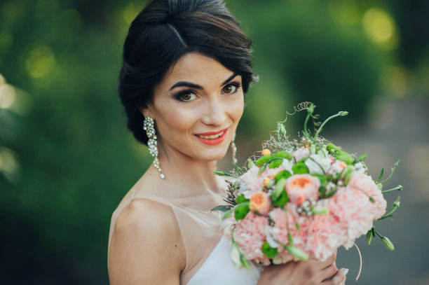 一个美丽的性感的年轻的黑发新娘在长长的白色婚纱和面纱站在森林里捧花在自然的背景，水平的图片图片下载