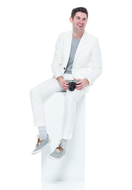 穿着白色衣服的帅气年轻人坐在白色的盒子上拿着相机图片下载