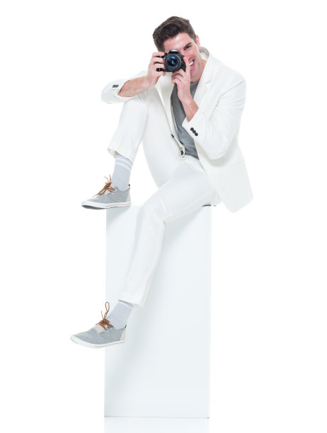 穿着白色衣服的帅气年轻人坐在白色的盒子上拿着相机图片下载