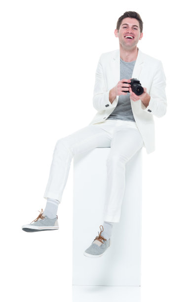 穿着白色衣服的帅气年轻人坐在白色的盒子上拿着相机图片下载