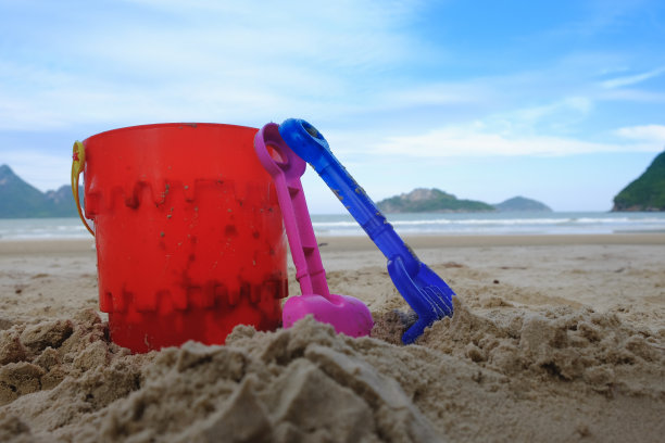 沙滩玩具桶、铁锹和铁铲放在沙滩上，以沙滩为背景图片下载