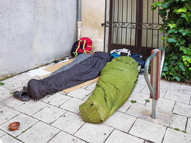 睡在城市人行道睡袋里的游客，城市贫困乞讨的旅行者图片下载