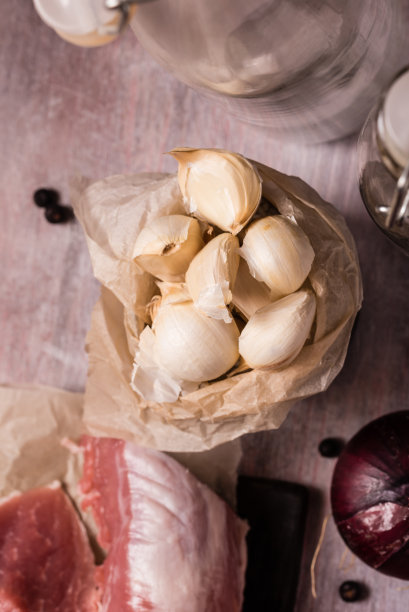 垂直照片与俯视图老罐满白蒜瓣。蔬菜放在老式的木板上，旁边是生的猪里脊肉和紫洋葱。图片下载