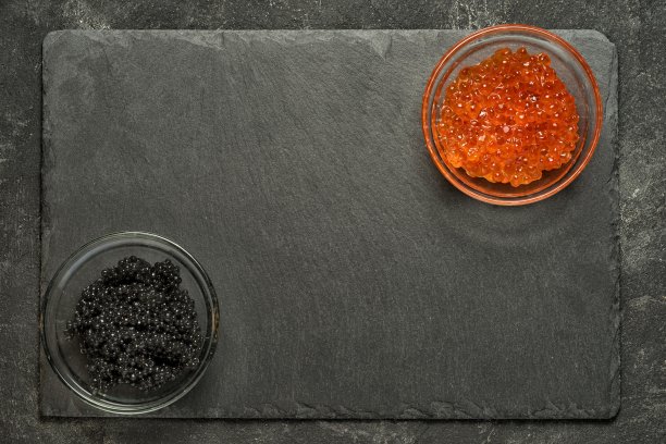 红鲑鱼和黑鲟鱼子酱在黑石板对面的角落，在一个黑色的桌子上，顶视图与拷贝空间。素材图片