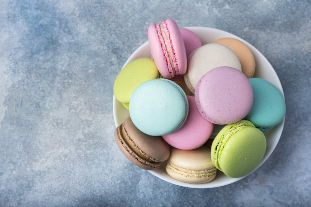 彩色马卡龙在一个白色的盘子上，在蓝色的背景。本空间素材图片