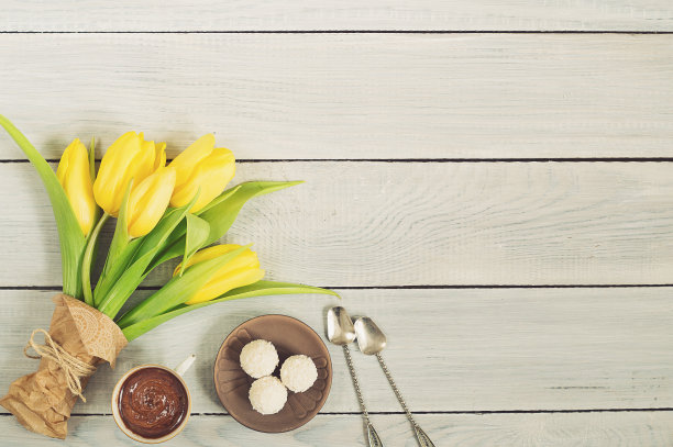 白色的木桌上放着黄色的郁金香、巧克力和糖果图片下载
