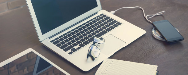 时尚和优雅的构成，为商务谈判或网站设计。智能手机、键盘、钱包、钢笔和眼镜的无线充电装置放在一张时尚复古的黑色办公桌上。图片下载