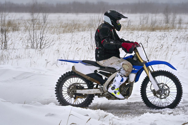 运动员、赛车手在极速公路上骑着摩托车飞驰。跑道很不平。多云的冬日里有暴风雪。图片下载