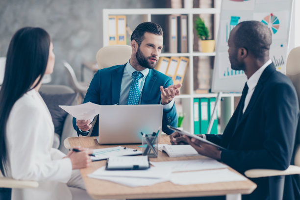 有吸引力的，英俊的，时尚的，优雅的男人在经典的西装解释一些东西给他的伙伴，三个同事坐在工作站，解决问题，找到解决方案，专业的结果图片下载