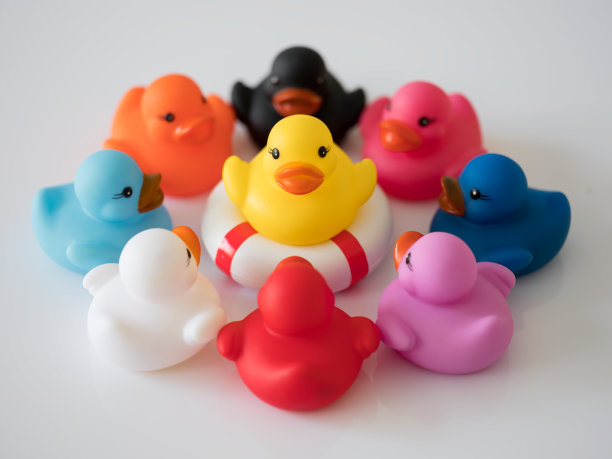 9只不同颜色的鸭子围成一个圈，彼此面对，场景设置在白色的背景上。图片下载