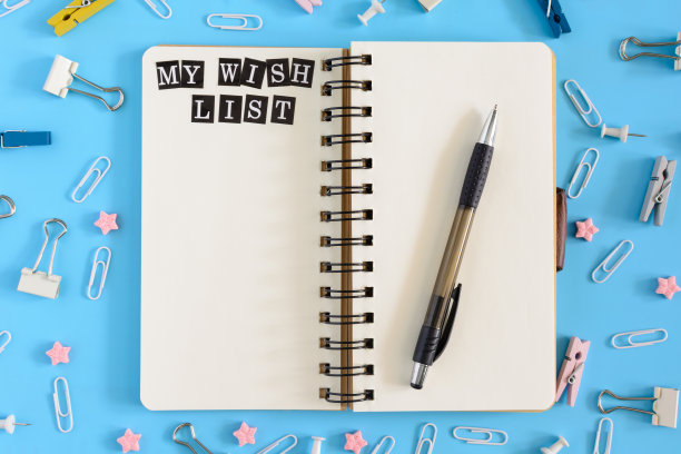 蓝色背景上杂乱的文具。中间放着一个打开的笔记本，上面是白纸。上面写着我的愿望清单。模拟。图片下载