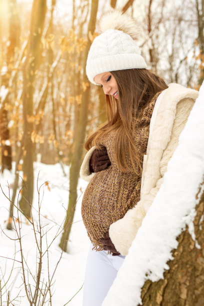 美丽的孕妇看着她的肚子在冬天的森林图片下载