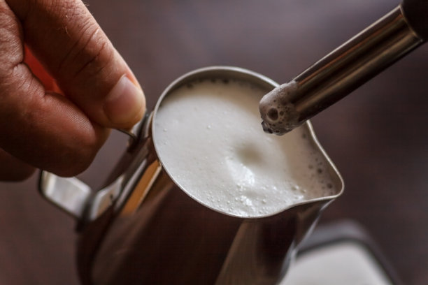 专业调酒师为卡布奇诺加热牛奶。咖啡师使用咖啡机制作玛奇朵拿铁艺术。健美的形象图片下载