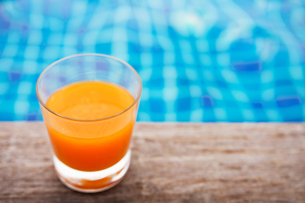 在夏天，橙汁在泳池边放松，蓝色绿松石池作为背景。Top View和Selective focus on glass图片下载