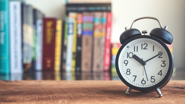 一个黑色闹钟的特写图像与模糊的书架在背景木桌子上图片下载