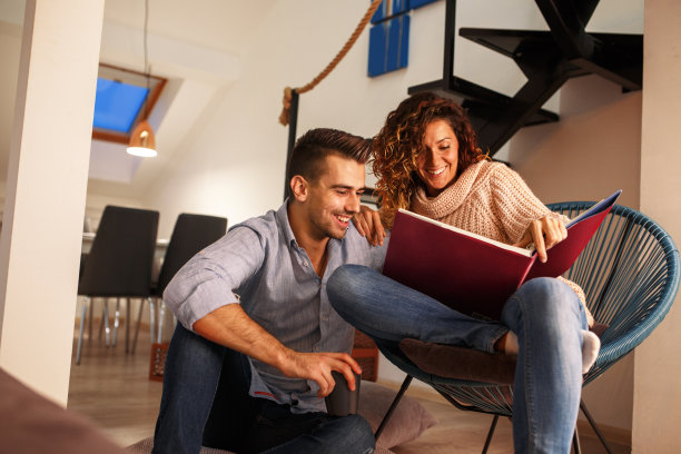 年轻夫妇看家庭相册。他们坐在客厅里喝咖啡。图片下载