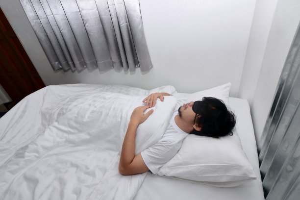 年轻的亚洲男子戴着眼罩睡在卧室的白色床上。图片下载