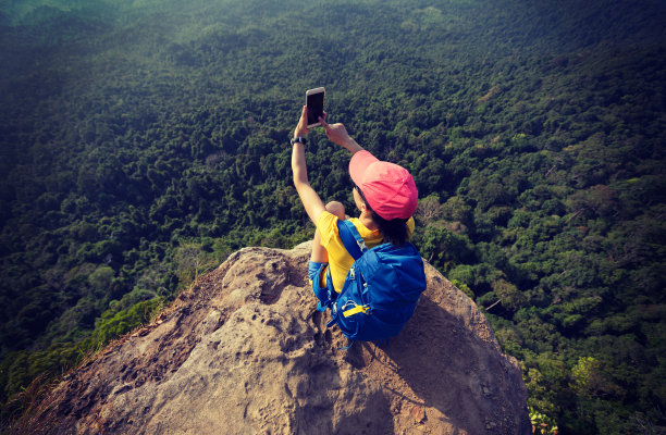 成功的女性徒步旅行者坐在悬崖边拍照图片下载