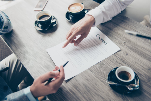近裁剪俯视图高角度照片的男人的手，将签署一份购买财产的协议。经纪人正在展示线把签名放在哪里，合伙人有咖啡喝图片下载