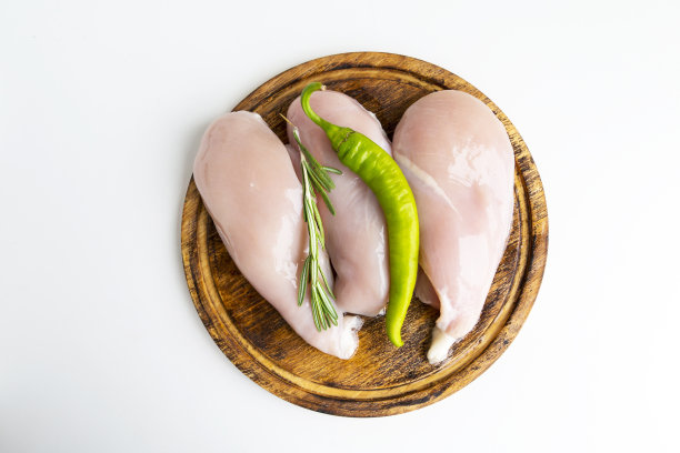 生鸡胸肉放在木板上，配上迷迭香药草和辣椒。图片下载