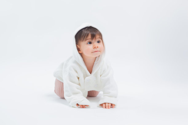 可爱的小女孩爬在睡袍坐在工作室在白色的背景图片下载
