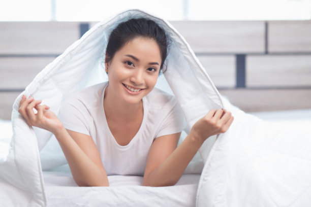 亚洲妇女从床上醒来，她用毯子和她的微笑。她是快乐的。图片下载