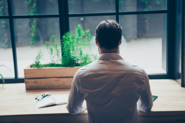 后视图的一个深色的记者时尚的家伙在白色经典衬衫，写一个故事在一个工作场所在阁楼共同工作，穿着很好，坐在靠近窗口与景观城市图片下载