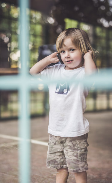 可爱的小男孩在窗边打电话。图片下载