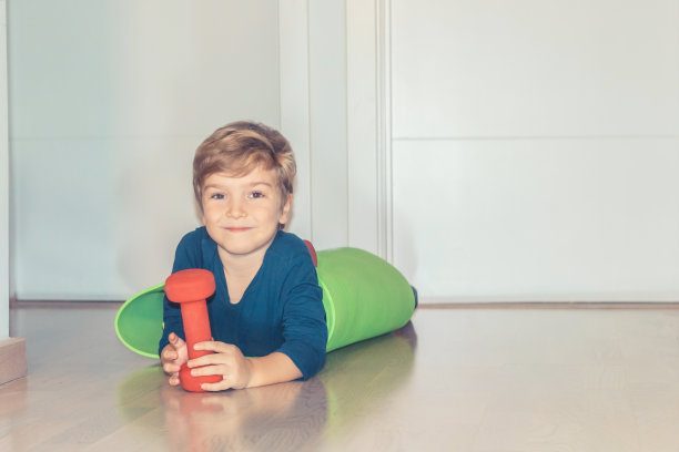 微笑的男孩手握重物，躺在地板上。图片下载