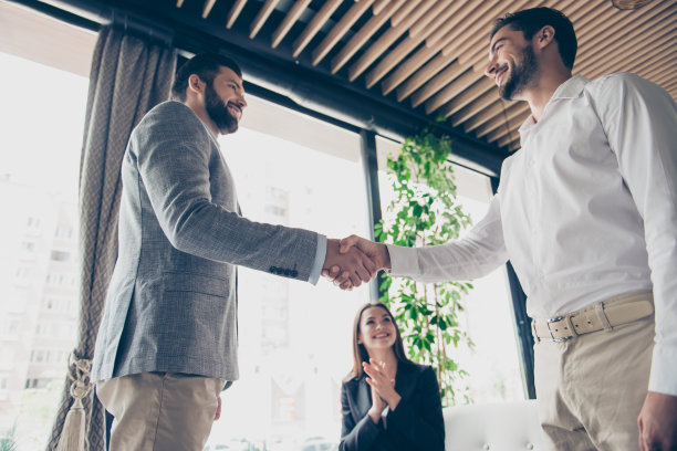 低角度照片的三个商业伙伴在正式的服装达成交易的业务。男人在握手完成交易，女人在高兴地拍手图片下载