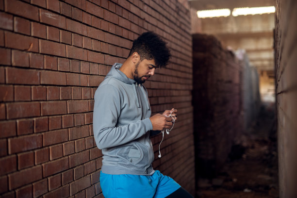 这是一幅充满激情的非裔美国年轻英俊的花花公子的肖像，他站在两堵墙中间的一个废弃的地方，准备训练用的耳机。图片下载