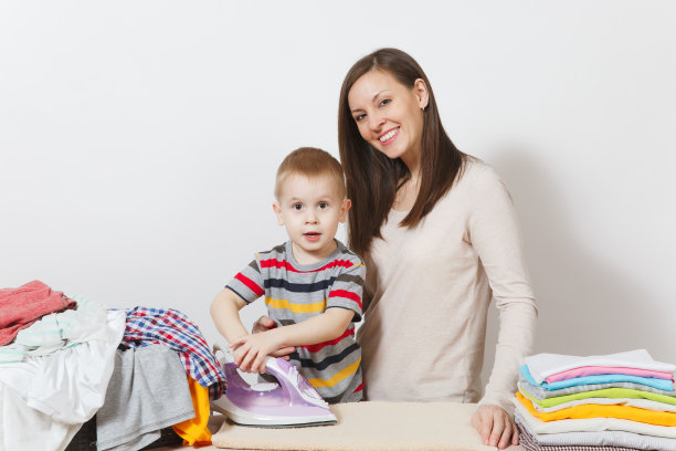 小男孩，女人在熨衣板上用熨斗烫衣服。儿子帮助母亲做家务孤立在白色的背景。鼓励儿童自主的观念。为人父母,孩子的概念。图片下载