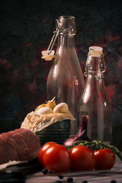 垂直照片与旧旧的罐头，这是充满白蒜瓣。罐头旁边是红色的樱桃番茄、整块里脊猪肉和老式玻璃瓶。图片下载