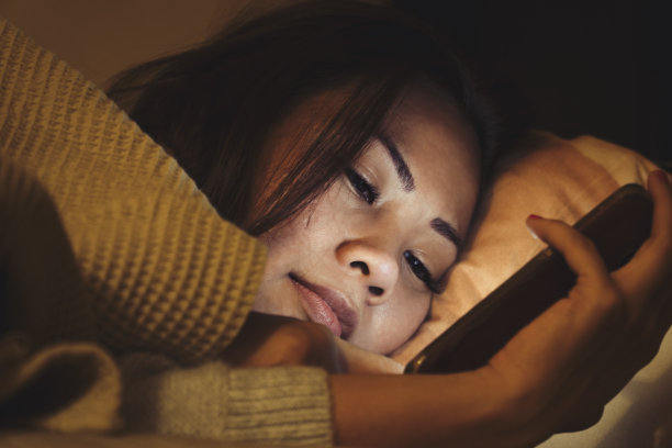 一个亚洲女人在床上玩手机图片下载