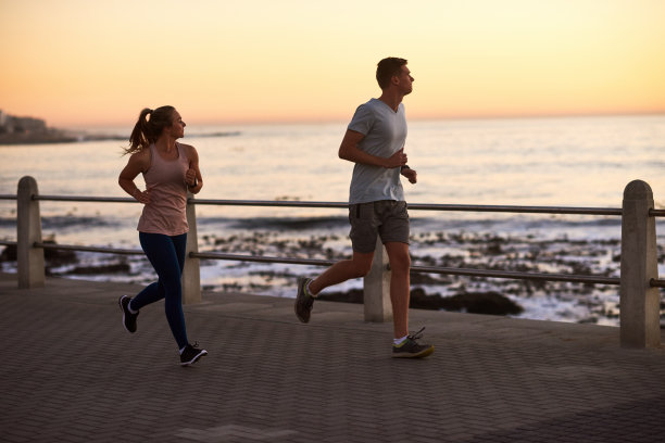 一对年轻的健康夫妇在日落时沿着海边慢跑图片下载